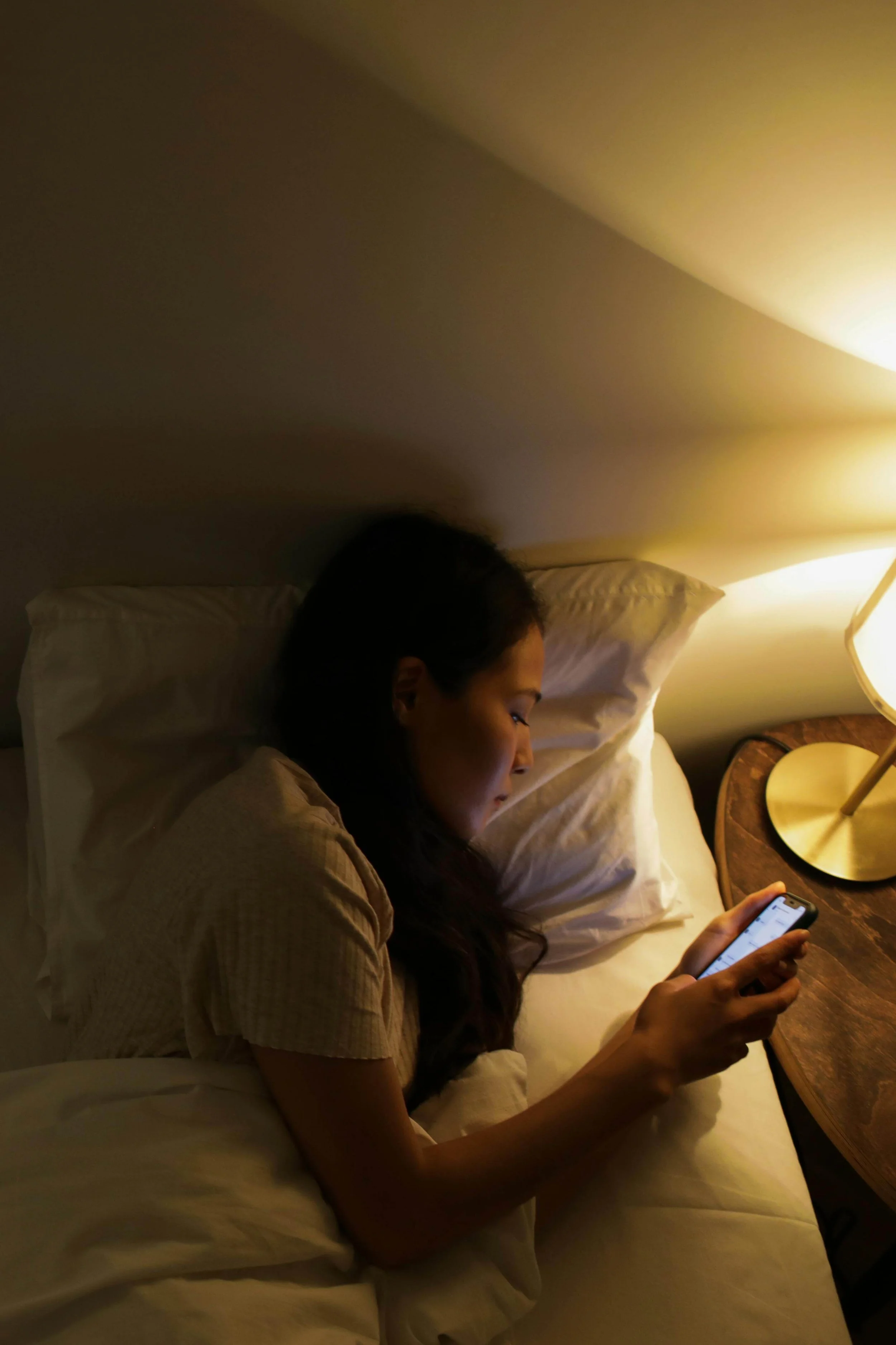 A woman laying awake in bed researching online near a lamp. ERP therapy for OCD in Boston, MA can help you with responding to physical compulsions in a new way. Learn more here!