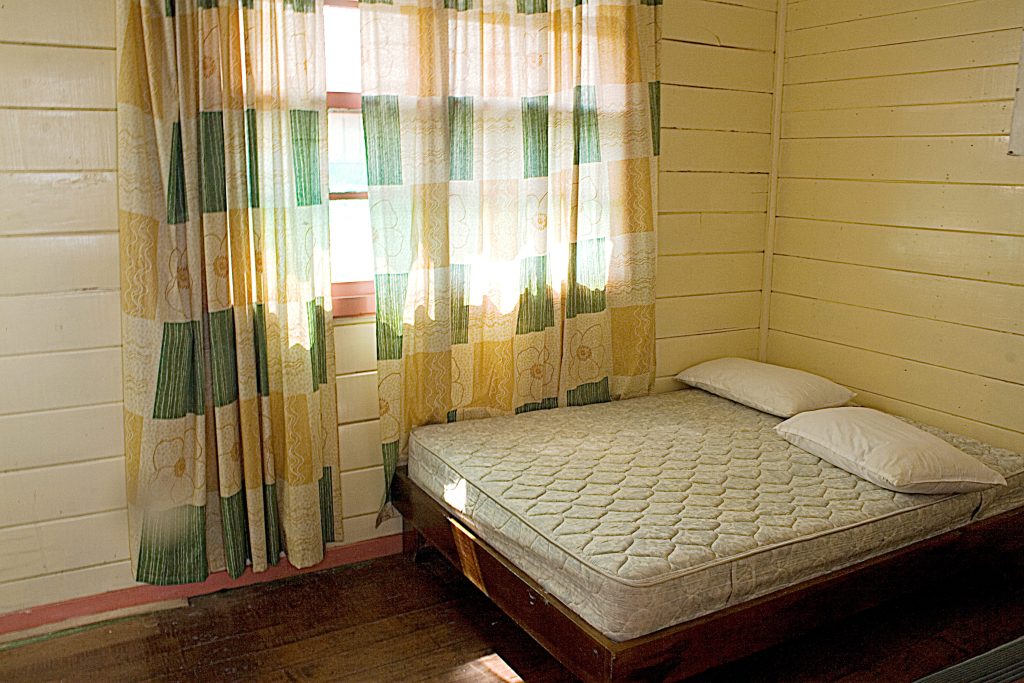 A bare bed in a well-lit room with bright yellow walls & a floral patterned curtains. OCD therapy in San Diego, CA can help you learn a new relationship with fear & uncertainty. Learn more here.